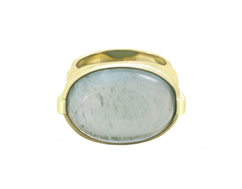 Large green gold ring with overlapping ribbon of gold around the band set with rectangle cabochon of aquamarine. Gem lies across the finger.