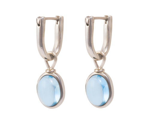 Oval drops with light blue cabochon gem in white gold frame. Drops hang on small U shaped hoops in solid white gold.