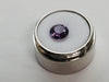 Medium round deep purple spinel gem, on white background in gem jar.