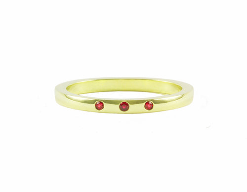 Thin green gold band set with three bright red round rubies. The gems are set into the band.