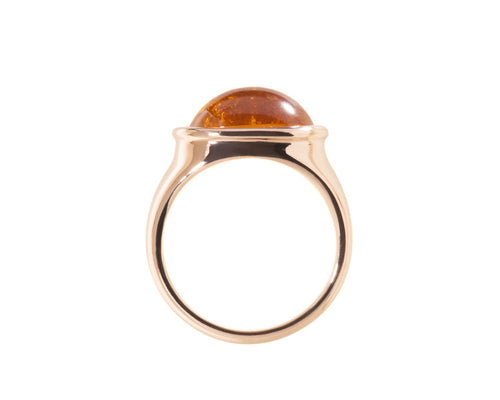 Rose gold ring set with medium oval cabochon of bright orange spessartite garnet. Gem is set in frame and lies across the finger.