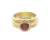 Deep orange round gem in green gold ring and matching green gold bands.