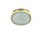 Large green gold ring with overlapping ribbon of gold around the band set with rectangle cabochon of aquamarine. Gem lies across the finger.