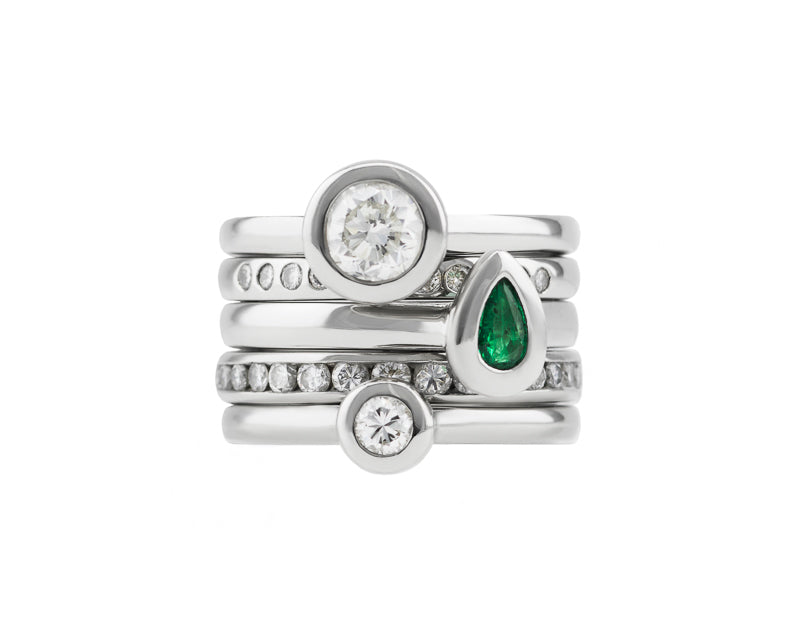 Stack of five platinum rings with diamonds and a pear-shape emerald.