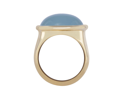 Green gold ring set with large oval cabochon of rich blue aquamarine. Gem is set in frame and lies across the finger.