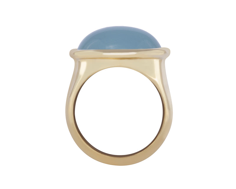 Green gold ring set with large oval cabochon of rich blue aquamarine. Gem is set in frame and lies across the finger.