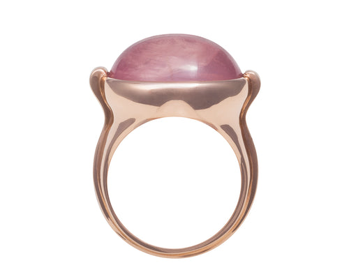 Large rose gold ring with overlapping ribbon of gold around the band set with large oval cabochon of rose quartz. Gem lies across the finger.
