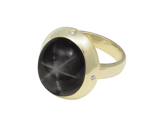 Very large round cabochon of deep grey star sapphire.  Gem is set in a skirt-like bezel with four accent diamonds.