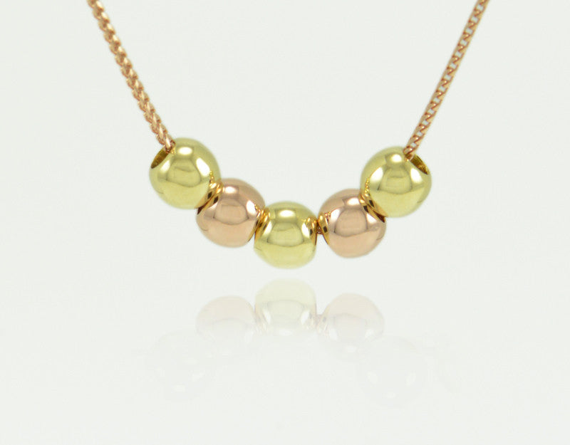 Five round beads in rose and green gold on chain.