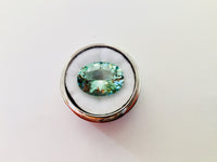Large oval green beryl gem, on white background in gem jar.
