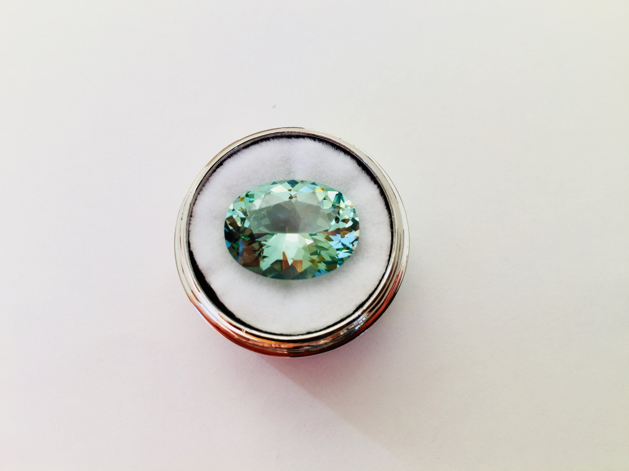 Large oval green beryl gem, on white background in gem jar.