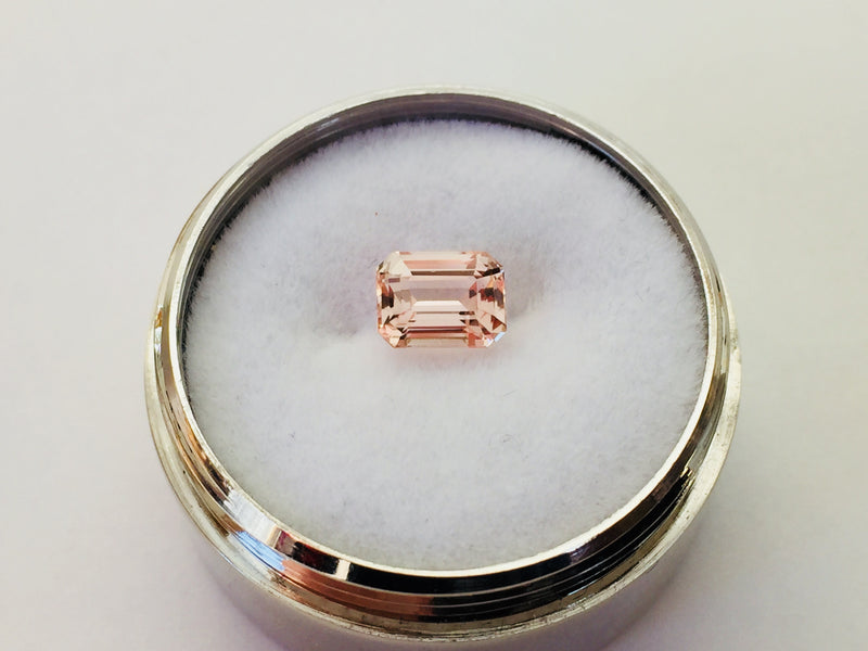 Small rectangular peach-pink sapphire gem, on white background in gem jar.