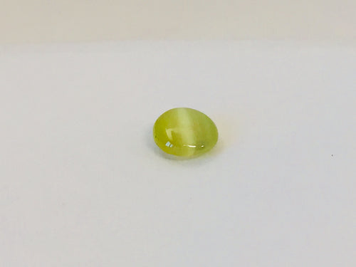 Small round green-yellow Cat's Eye Chrysoberyl gem with white stripe across centre, white background.