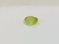 Small round green-yellow Cat's Eye Chrysoberyl gem with white stripe across centre, white background.