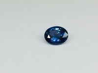 Small oval deep blue spinel gem, white background.