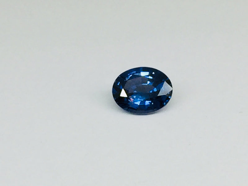 Small oval deep blue spinel gem, white background.