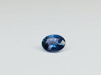 Small oval deep blue spinel gem, white background.