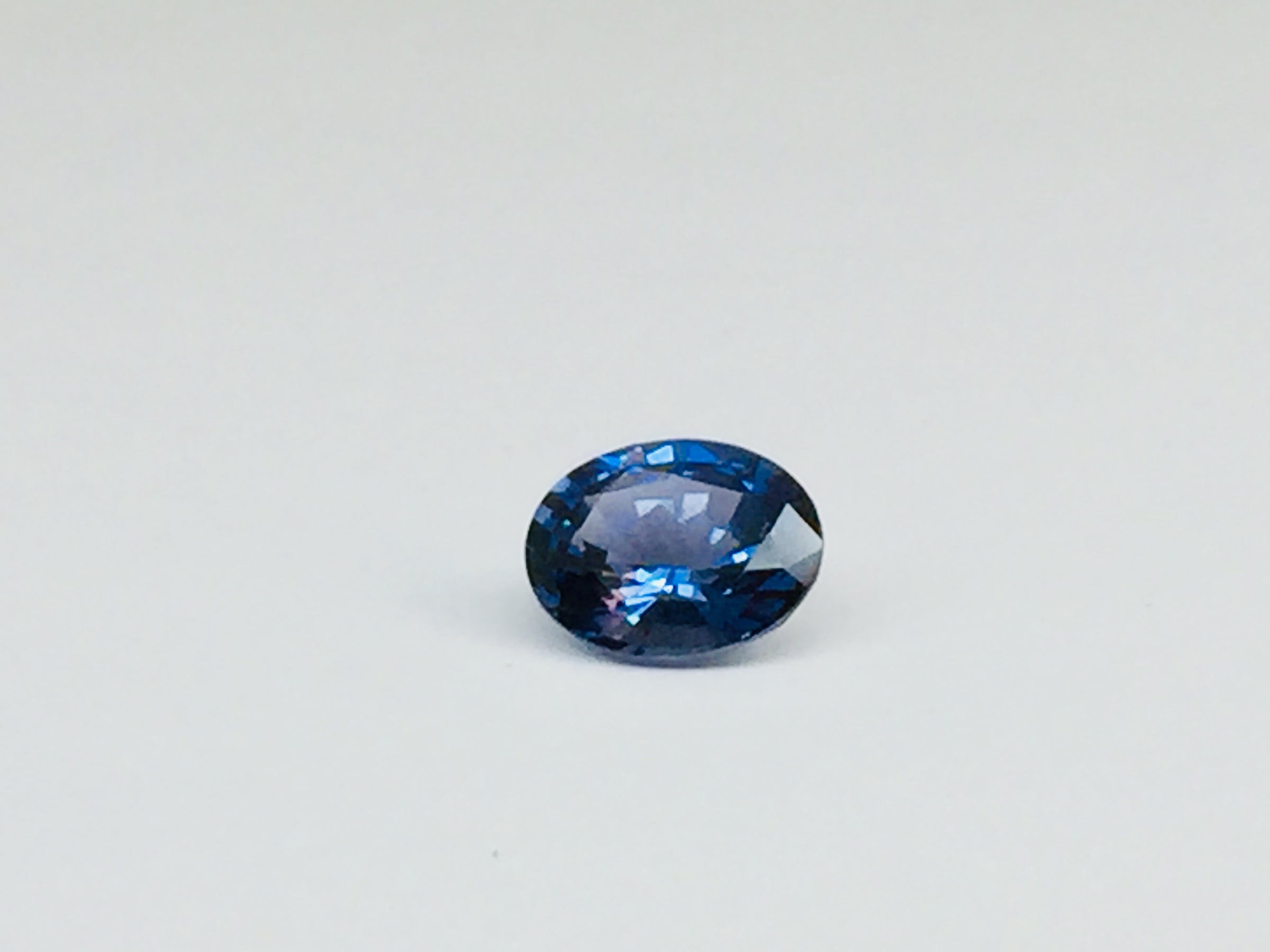 Small oval deep blue spinel gem, white background.