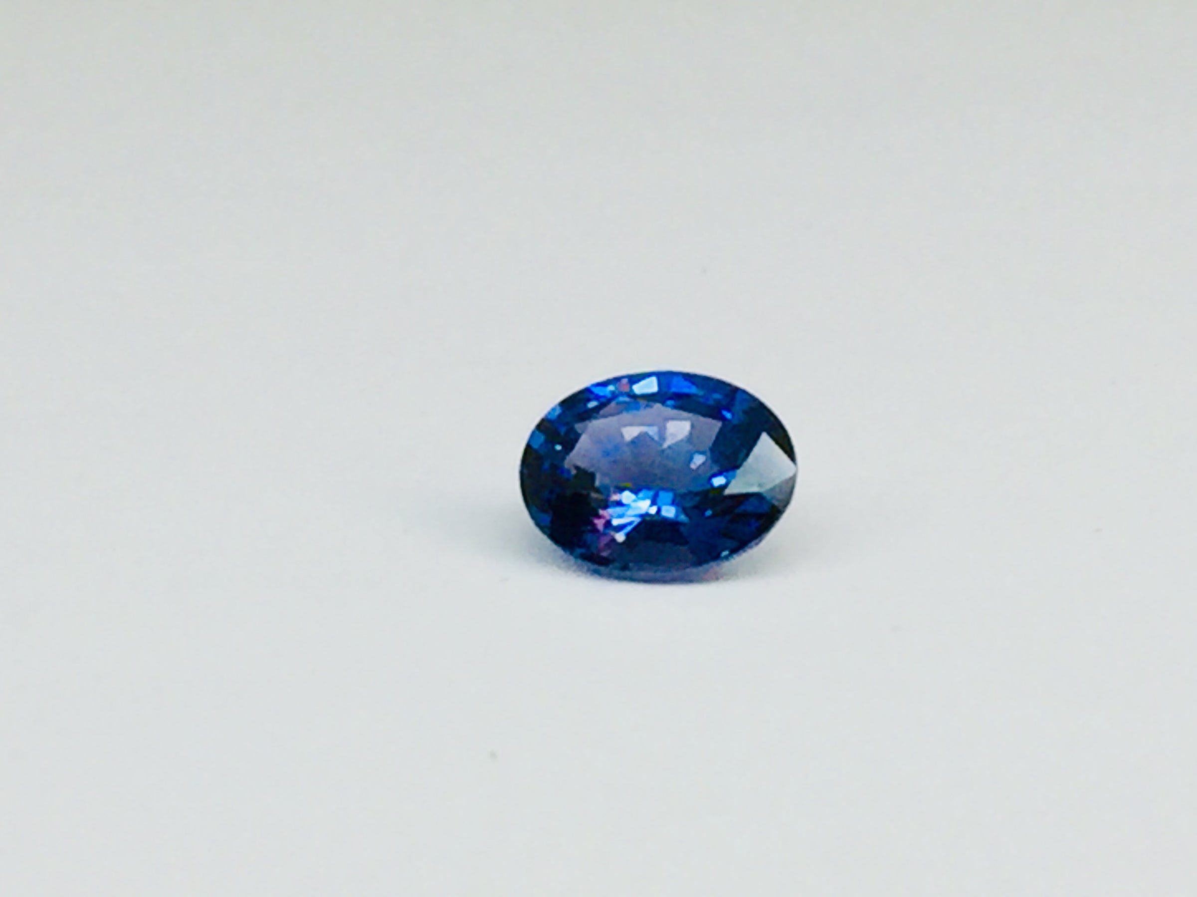 Small oval deep blue spinel gem, white background.