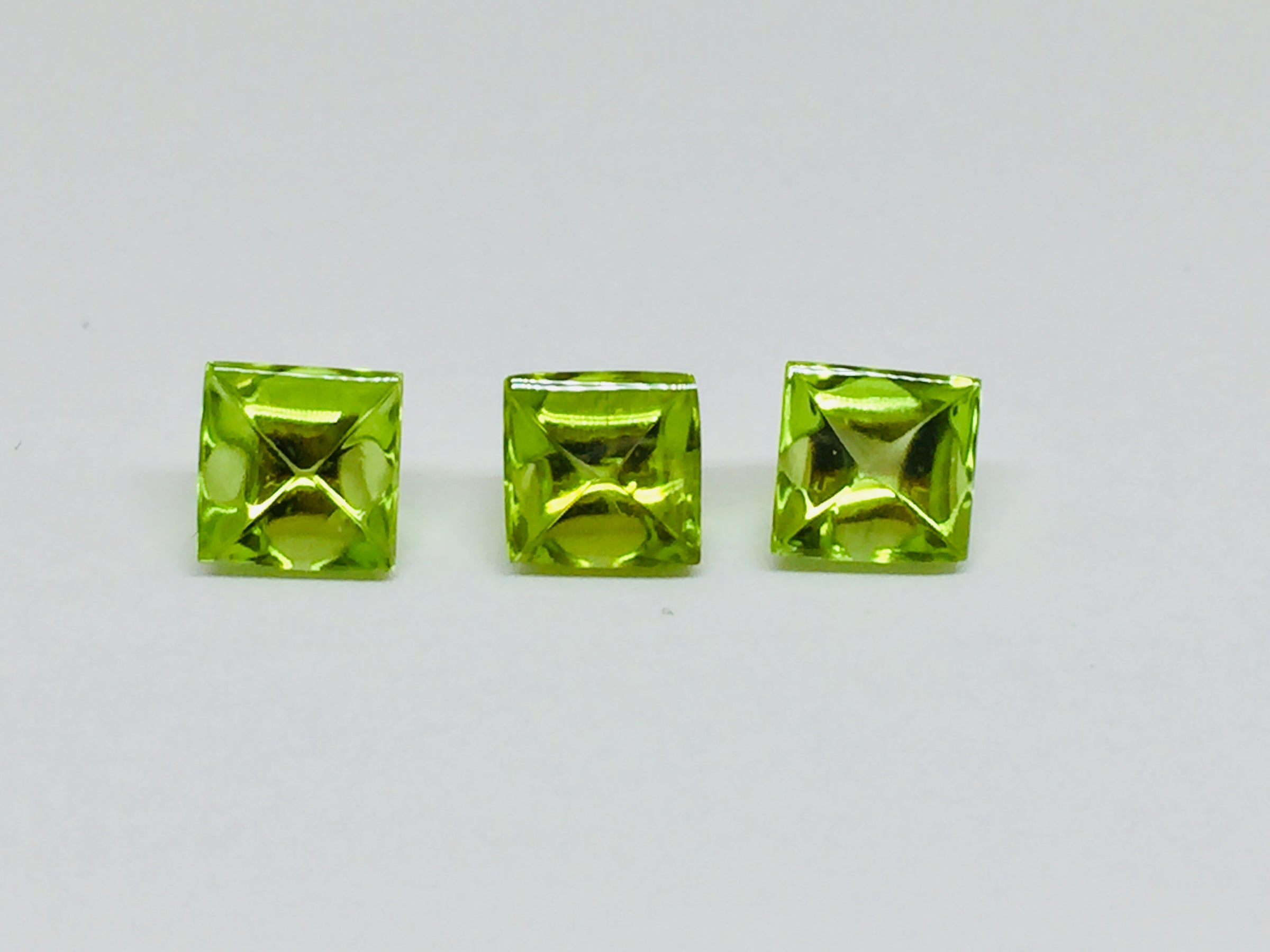 Three buff top peridot gems, white background.