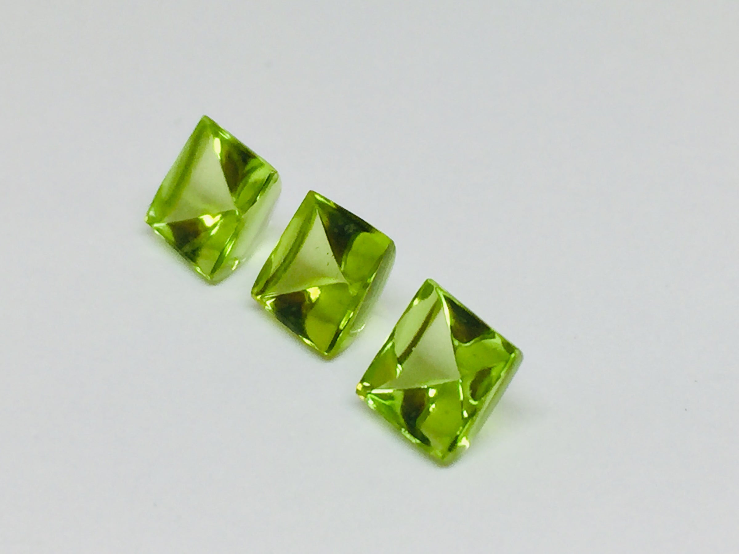 Three buff top peridot gems, white background.