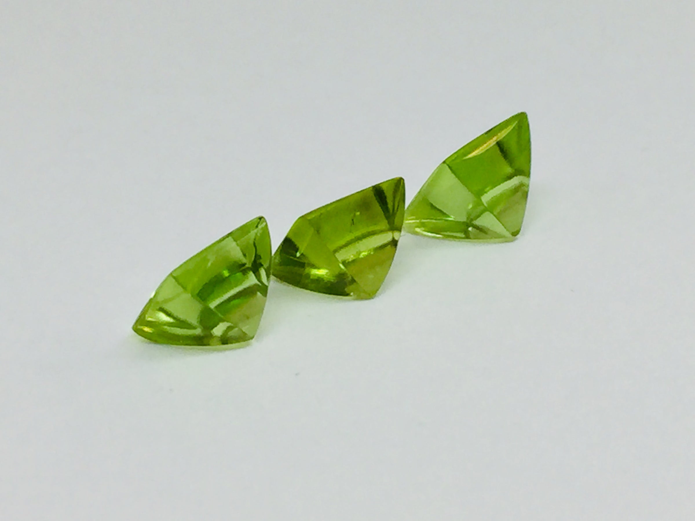 Three buff top peridot gems, white background.