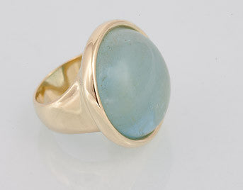 Very large green gold ring set with large round cabochon of blue aquamarine. Gem is set in frame and goes beyond width of finger.