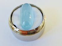 Long light blue aquamarine gem, white background in gem jar.