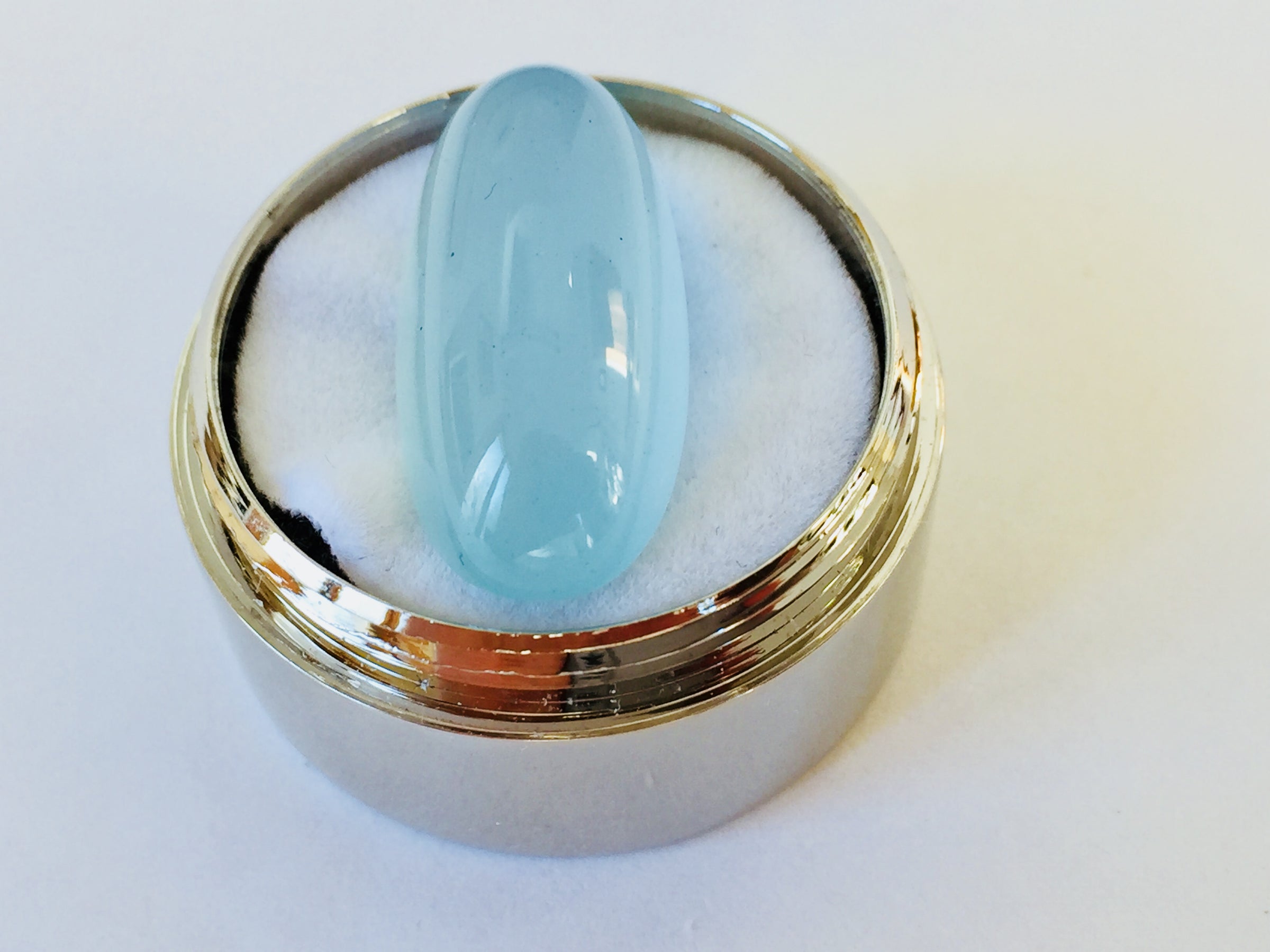 Long light blue aquamarine gem, white background in gem jar.
