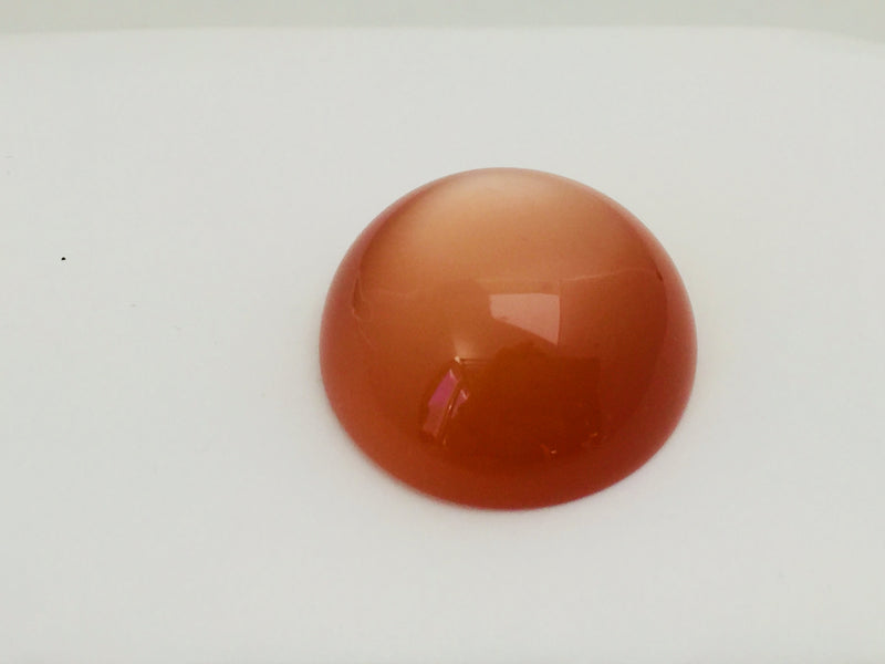 Very large round orange moonstone cabochon gem, white background.