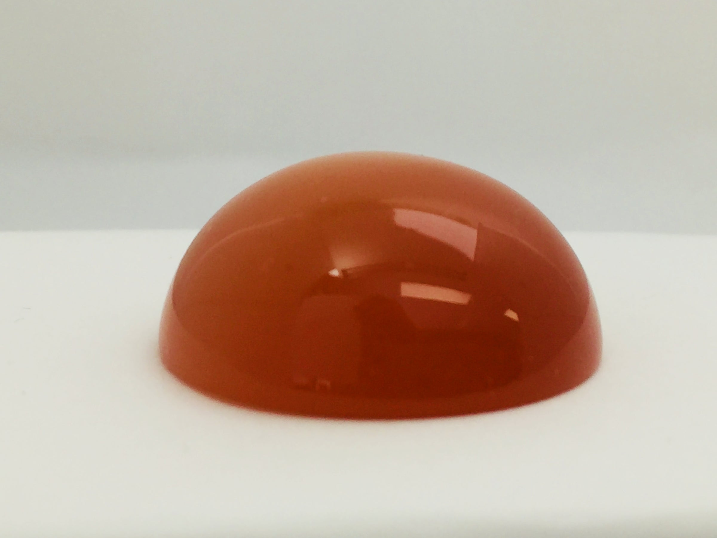 Very large round orange moonstone cabochon gem, white background.