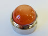 Very large round orange moonstone cabochon gem, white background, in gem jar.