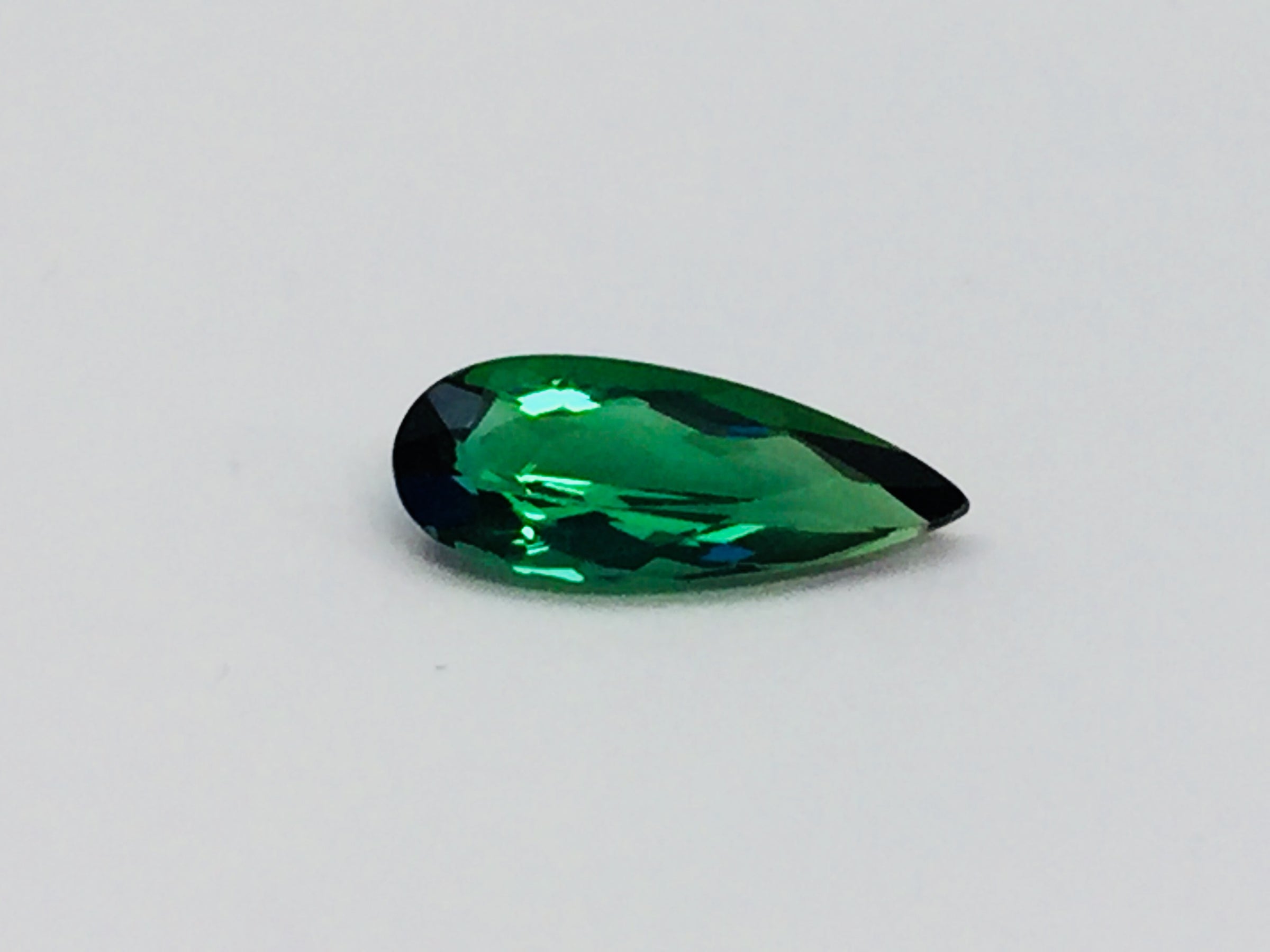 Small pear shape green tourmaline gem, white background.