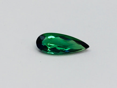 Small pear shape green tourmaline gem, white background.