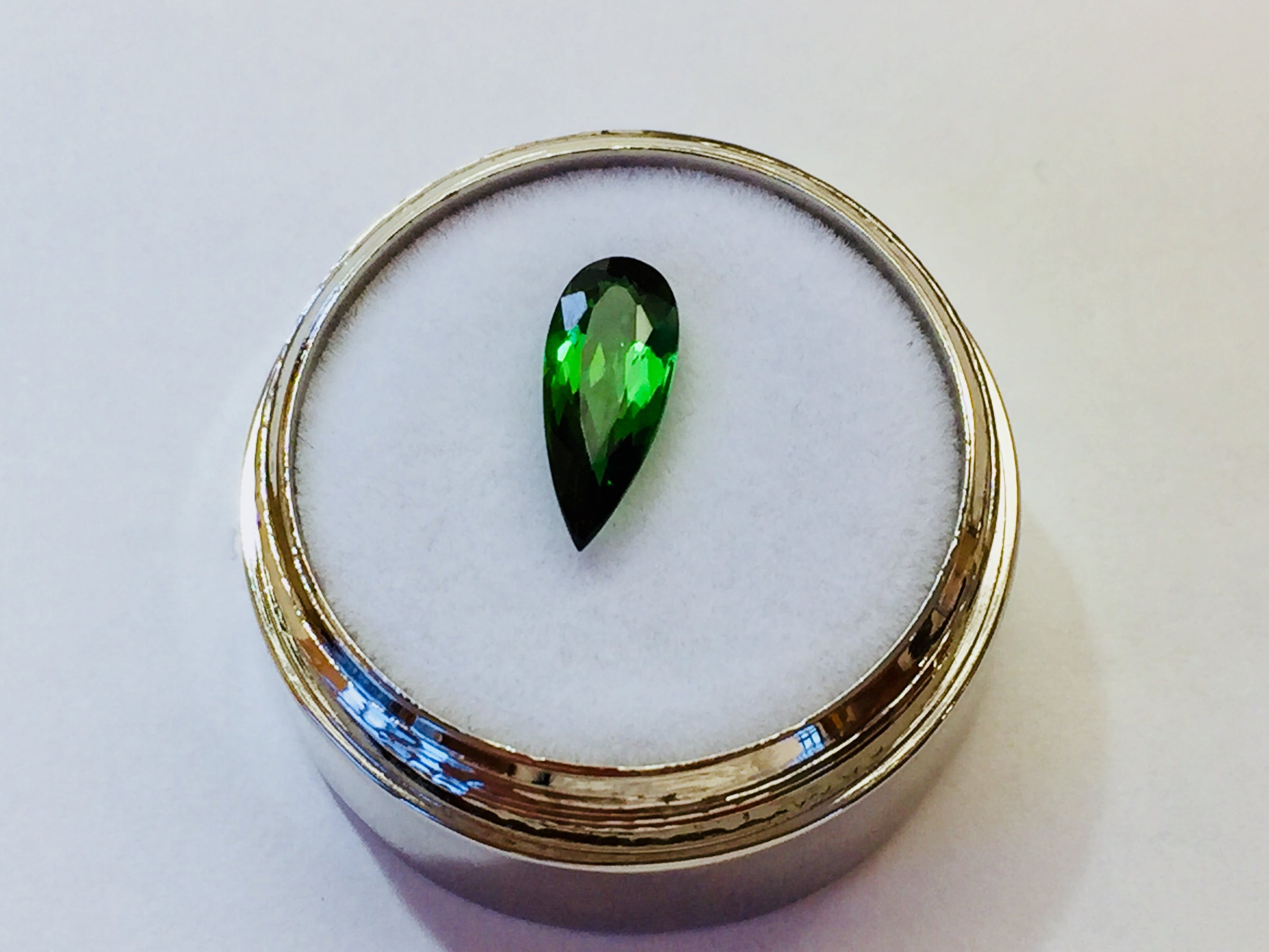 Small pear shape green tourmaline gem, white background.