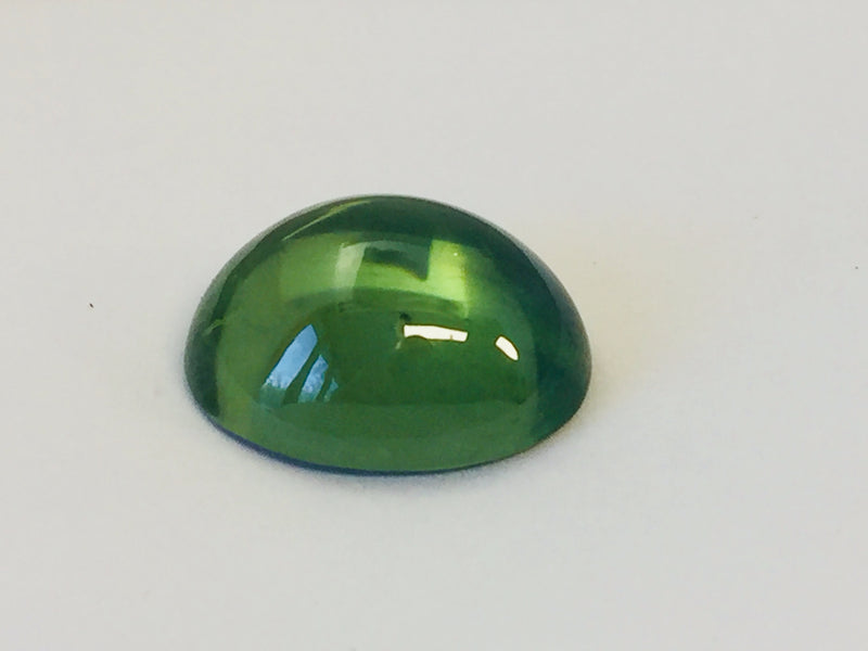 Large oval rich green zircon cabochon gem, white background.