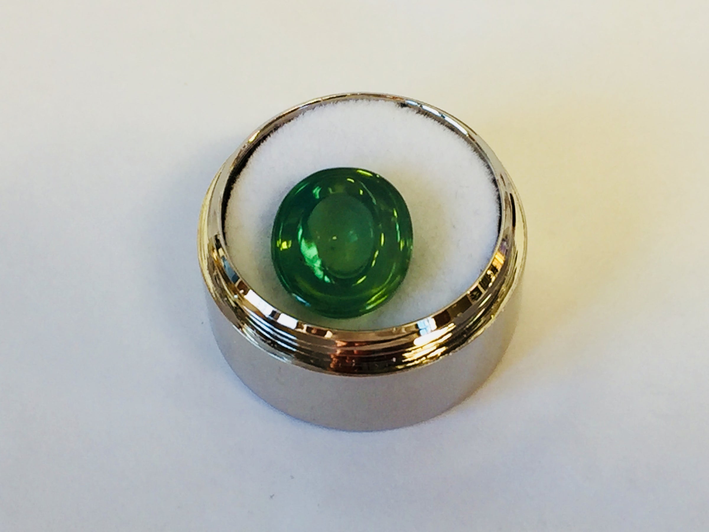 Large oval rich green zircon cabochon gem, white background in gem jar.