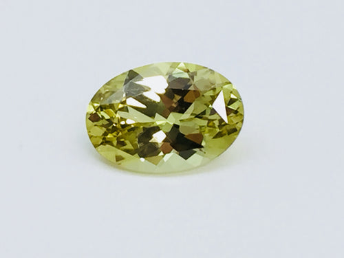 Oval light green- yellow chrysoberyl gem, on white background.