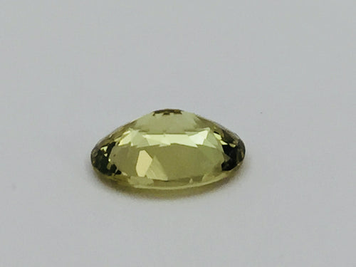 Oval light green- yellow chrysoberyl gem, on white background.