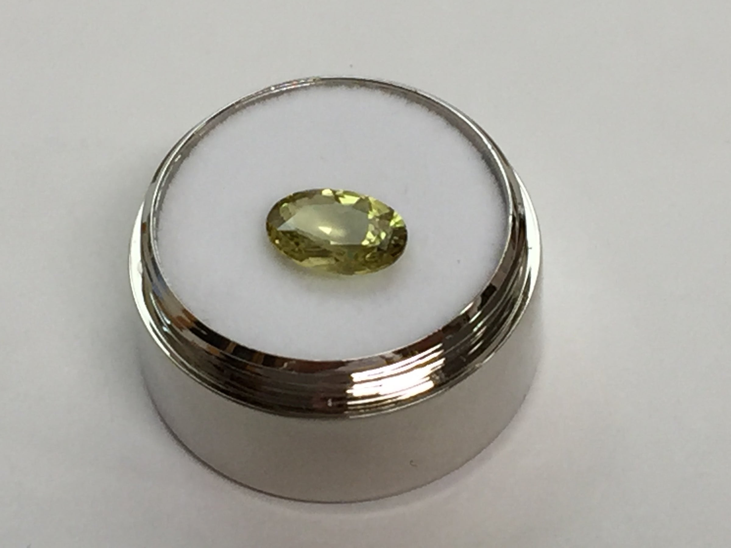 Oval light green- yellow chrysoberyl gem, on white background in gem jar.