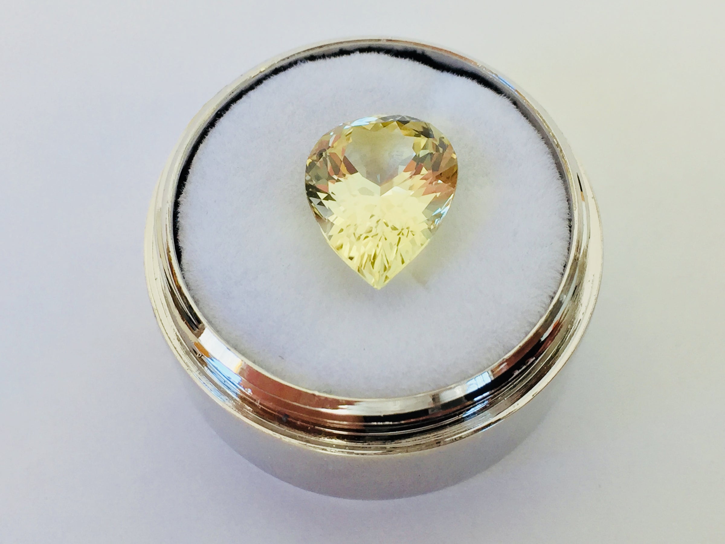 Large pear shaped light yellow chrysoberyl gem, on white background in gem jar.