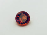 Medium round deep orange spessartite garnet gem, white background.