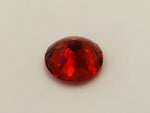 Medium round deep orange spessartite garnet gem, white background.