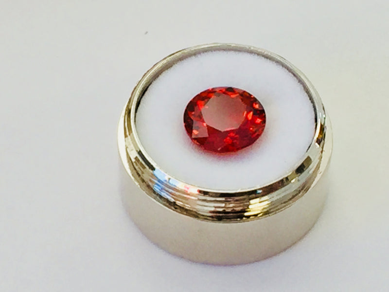 Medium round deep orange spessartite garnet gem, white background in gem jar.