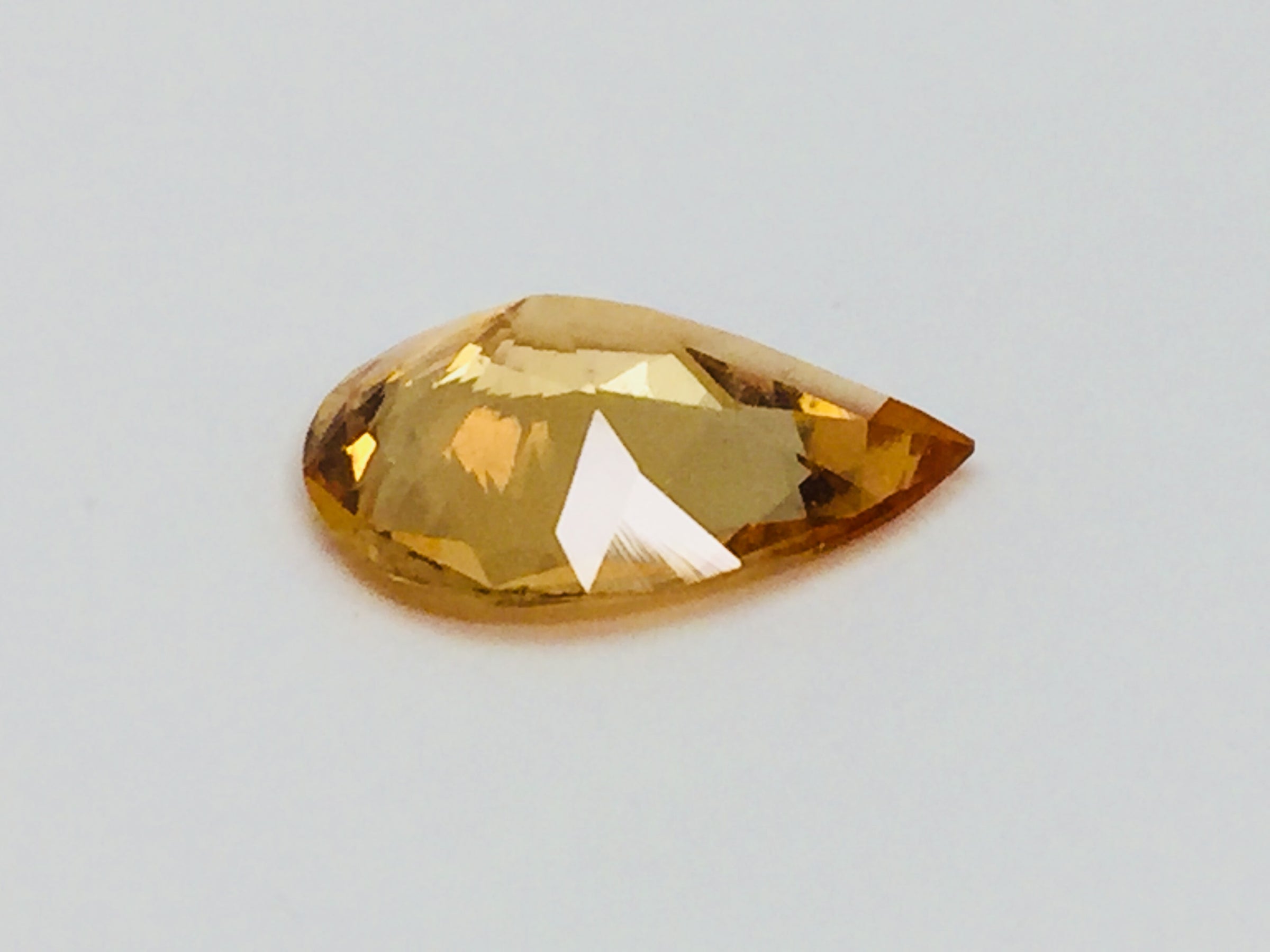 Large pear shaped orange hessonite garnet gem, on white background.