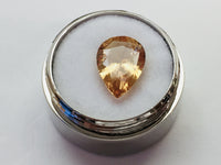 Large pear shaped orange hessonite garnet gem, on white background in gem jar.