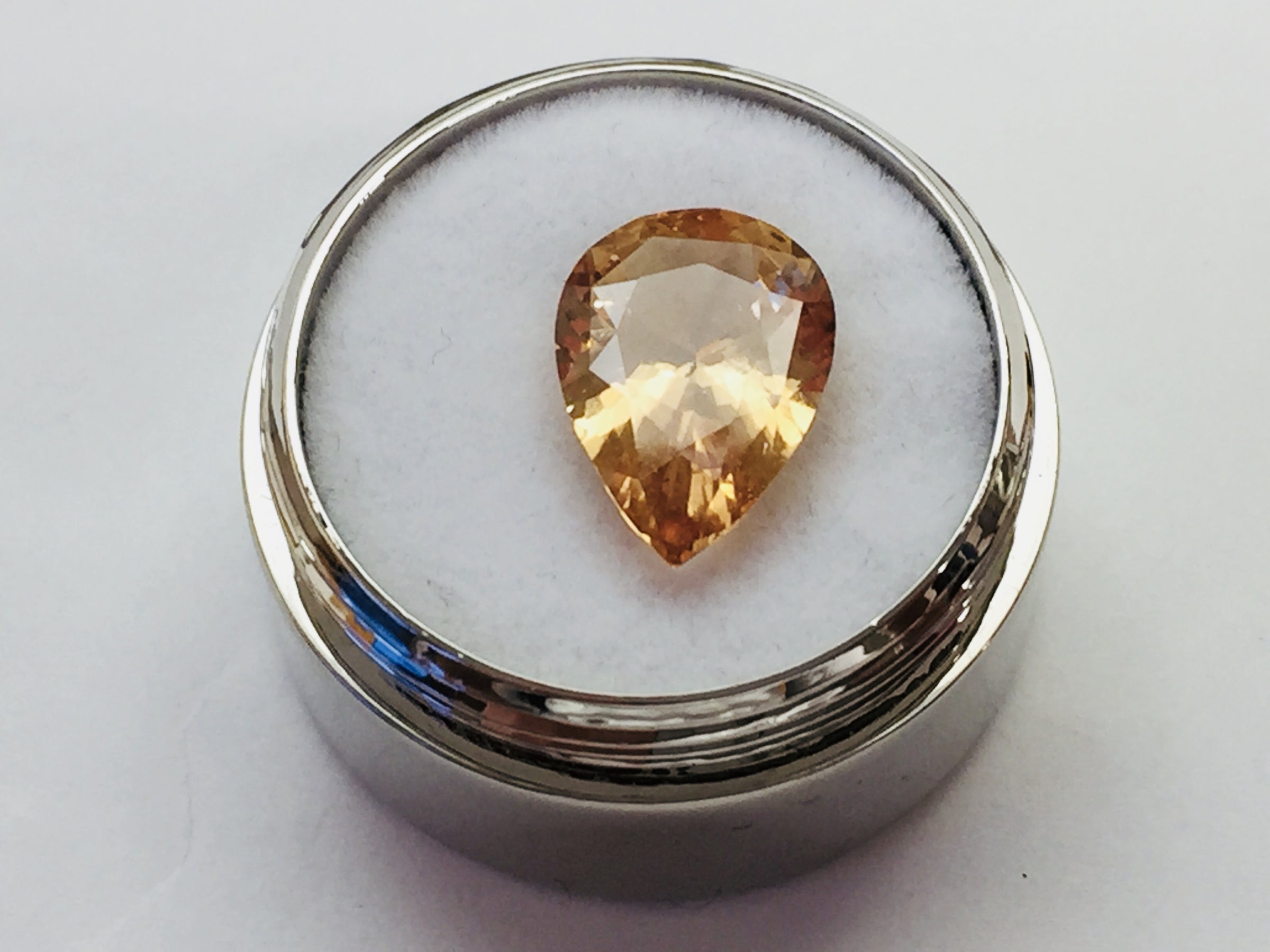 Large pear shaped orange hessonite garnet gem, on white background in gem jar.