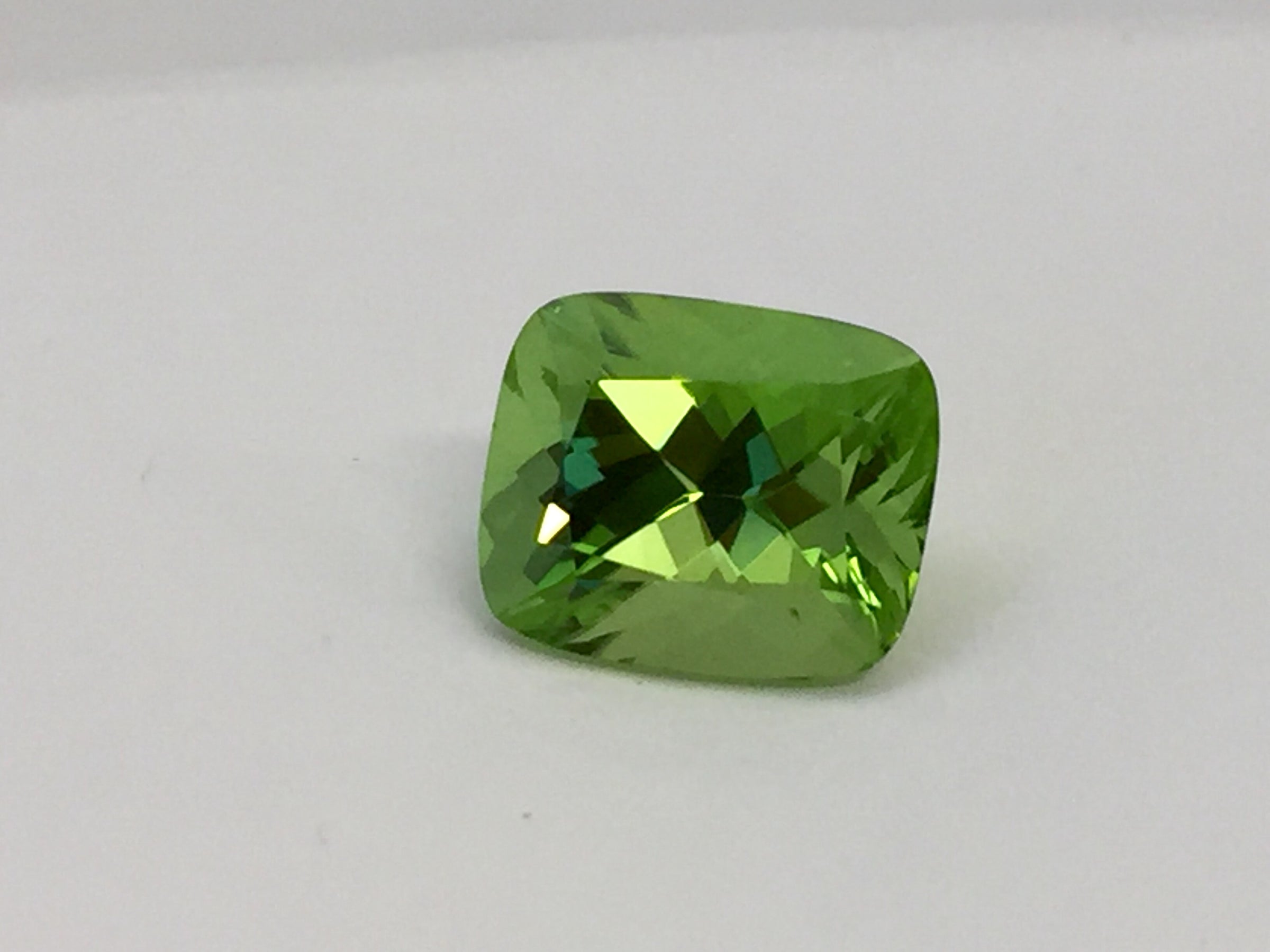 Large deep green cushion shaped peridot gem, white background.