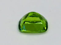 Large deep green cushion shaped peridot gem, white background.