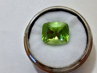 Large deep green cushion shaped peridot gem, white background in gem jar.
